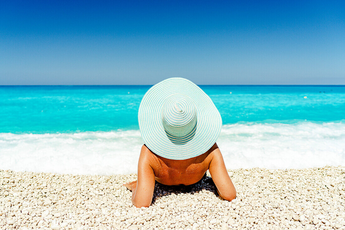 Unbekümmerte Frau mit Strohhut beim Sonnenbaden an einem idyllischen Strand, Kefalonia, Ionische Inseln, Griechische Inseln, Griechenland, Europa