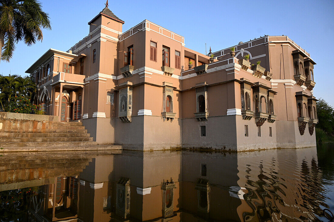 Annäherung an Sri Joravar Vilas, das sich bei Sonnenuntergang im Wasser des Sees spiegelt, an dem es steht, Santrampur, Gujarat, Indien, Asien