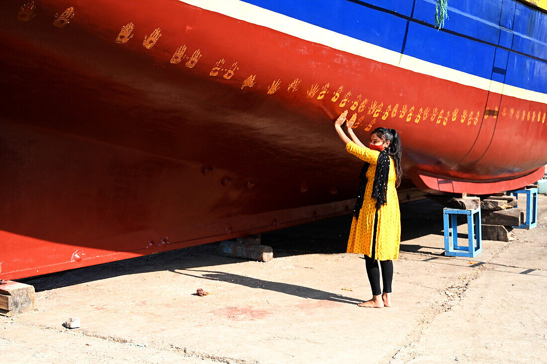 Die Tochter des Bootseigentümers vollzieht eine Puja auf dem neuen Boot, indem sie vor dem ersten Stapellauf Handabdrücke auf den Rumpf macht, Vanakbara, Gujarat, Indien, Asien