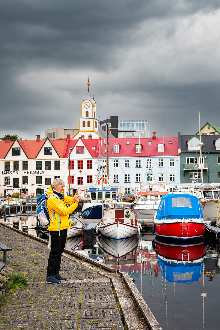 Ein Tourist macht ein Foto mit einem Smartphone vom Pier des Hafens von Torshavn, Streymoy Insel, Färöer Inseln, Dänemark, Europa