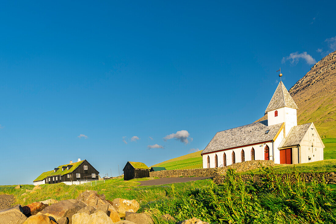 View of the church and grass roof houses among green meadows of Vidareidi, Vidoy island, Faroe Island, Denmark, Europe