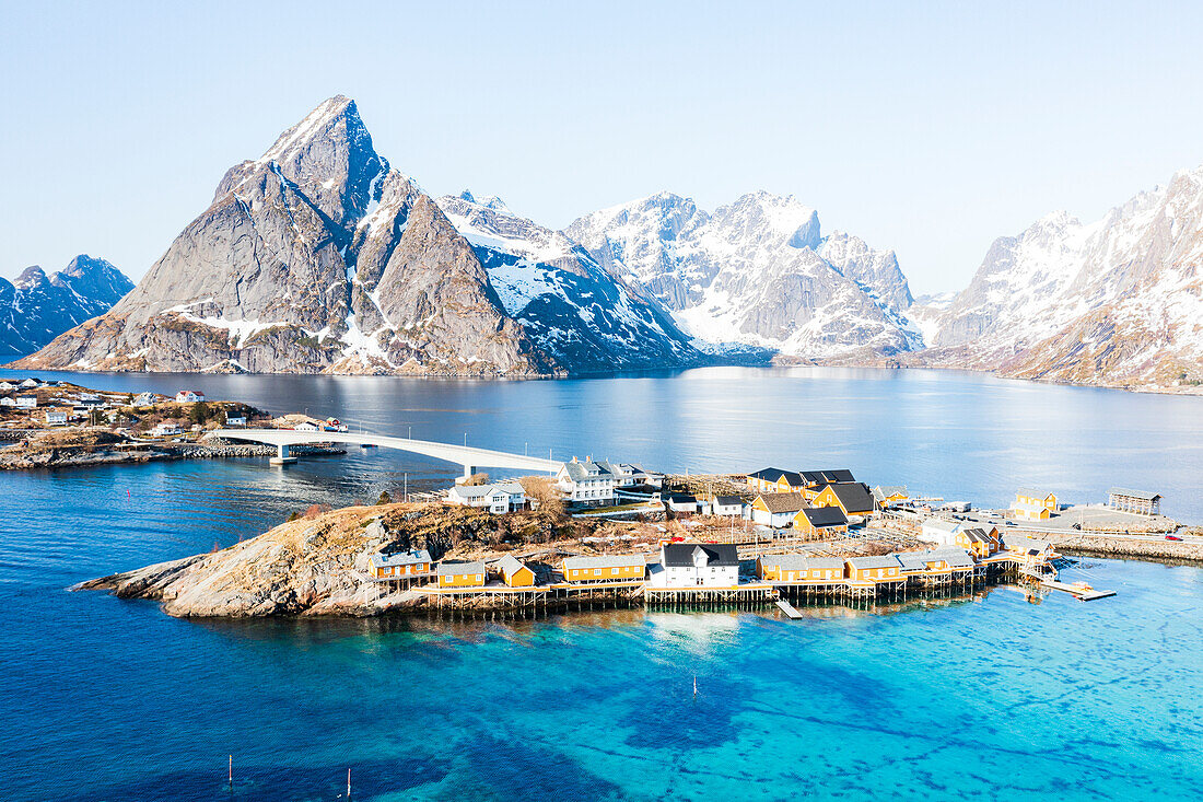 Luftaufnahme des Olstind-Gipfels und des türkisfarbenen Meeres, das das Dorf Sakrisoy und die Bucht von Reine umgibt, Lofoten-Inseln, Norwegen, Skandinavien, Europa