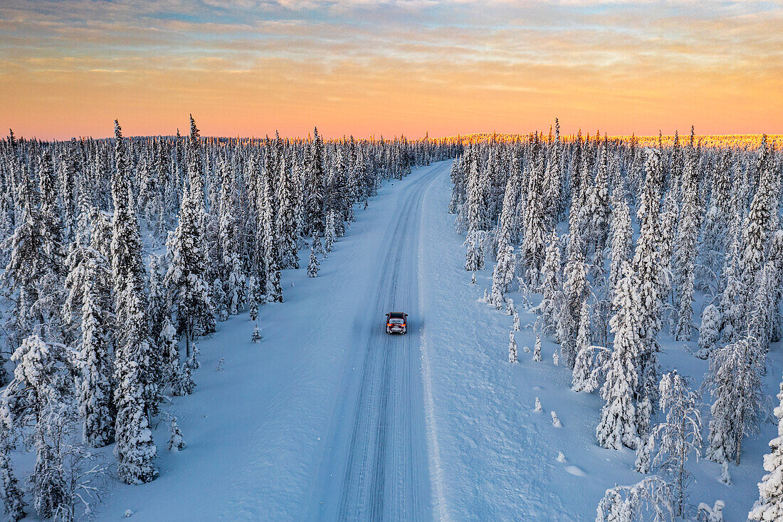 Dramatic sky at dawn over a car traveling into the snowy forest, aerial view, Kangos, Norrbotten County, Lapland, Sweden, Scandinavia, Europe