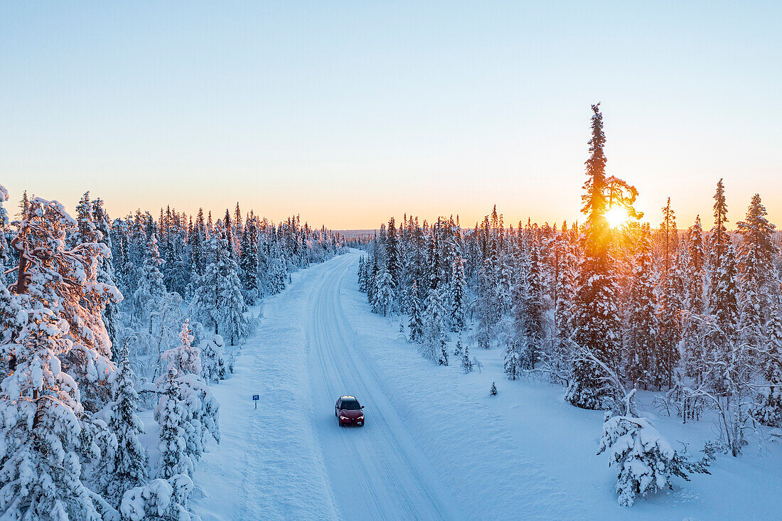 Auto auf einer verschneiten Straße im gefrorenen Wald bei Sonnenaufgang, Luftaufnahme, Kangos, Norrbotten County, Lappland, Schweden, Skandinavien, Europa