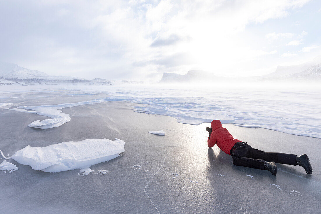 Mann fotografiert die verschneite Landschaft liegend auf einem zugefrorenen See, Stora Sjofallet, Norrbotten County, Lappland, Schweden, Skandinavien, Europa
