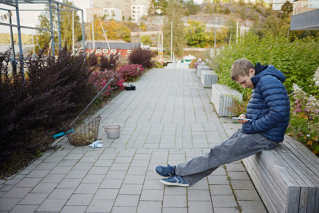 Jugendlicher sitzt auf einer Bank und benutzt sein Handy