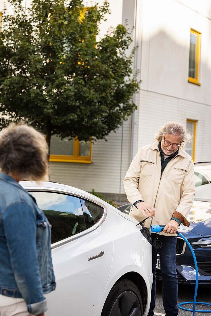 Senior man charging electric car outdoors