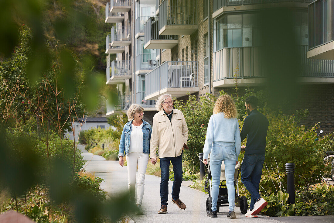 Senior and young couple with baby stroller walking in residential area