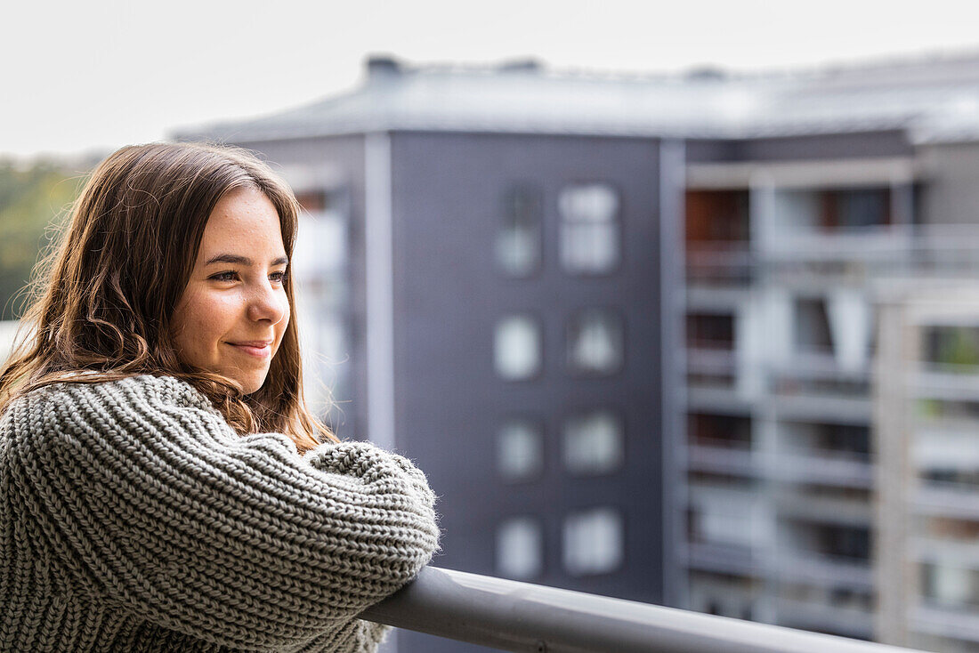 Lächelndes Teenager-Mädchen blickt vom Balkon auf die Aussicht