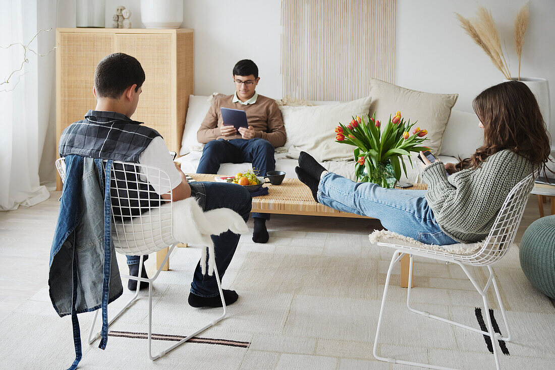 Teenager sitzen im Wohnzimmer und benutzen Handy und Tablet