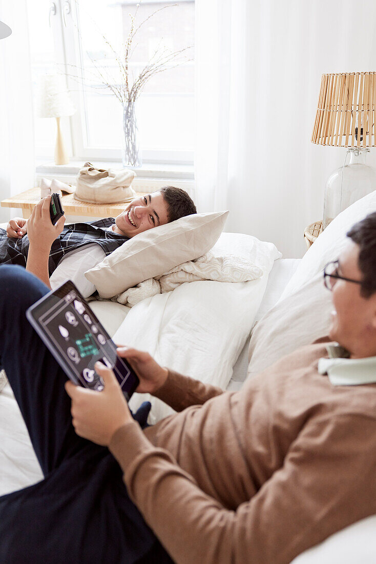 Brüder liegen auf dem Bett und benutzen Telefon und Tablet