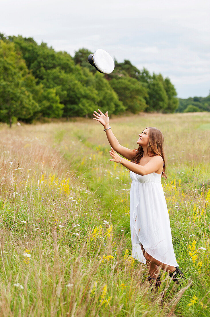 Young woman throwing hat in field