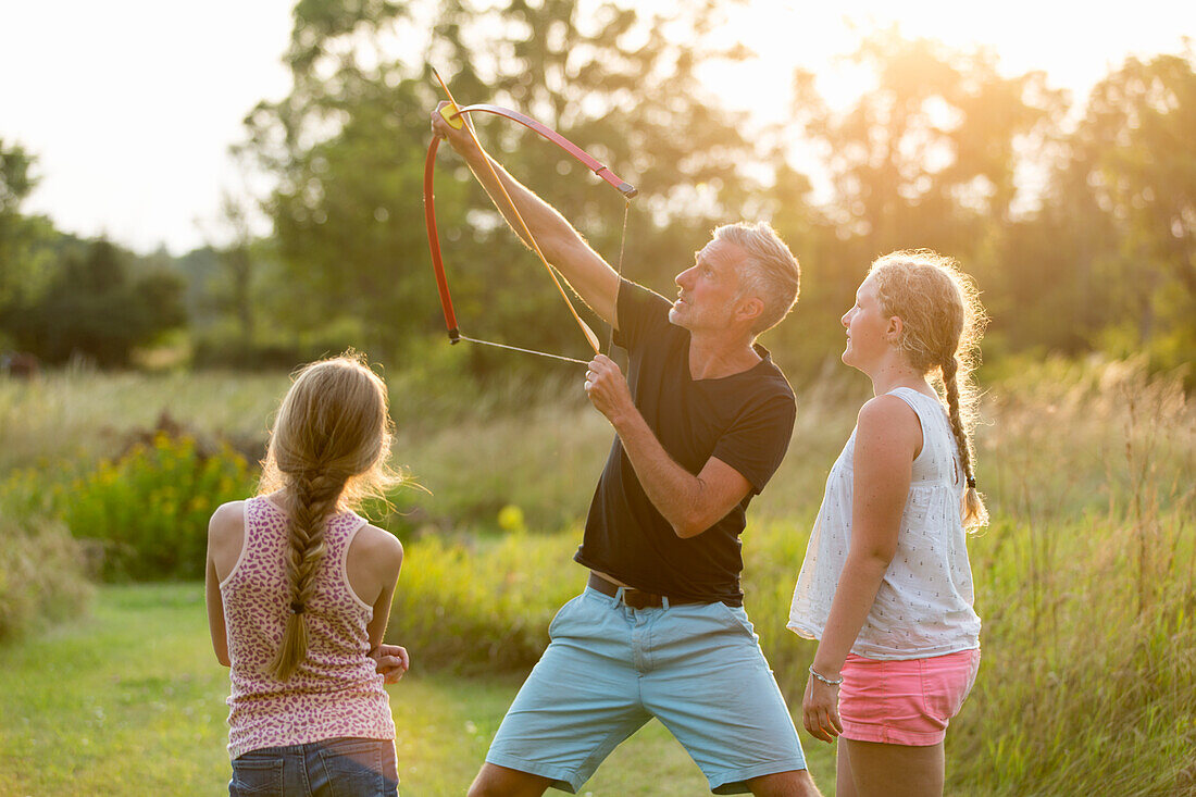 Father showing daughters how to use bow and arrows