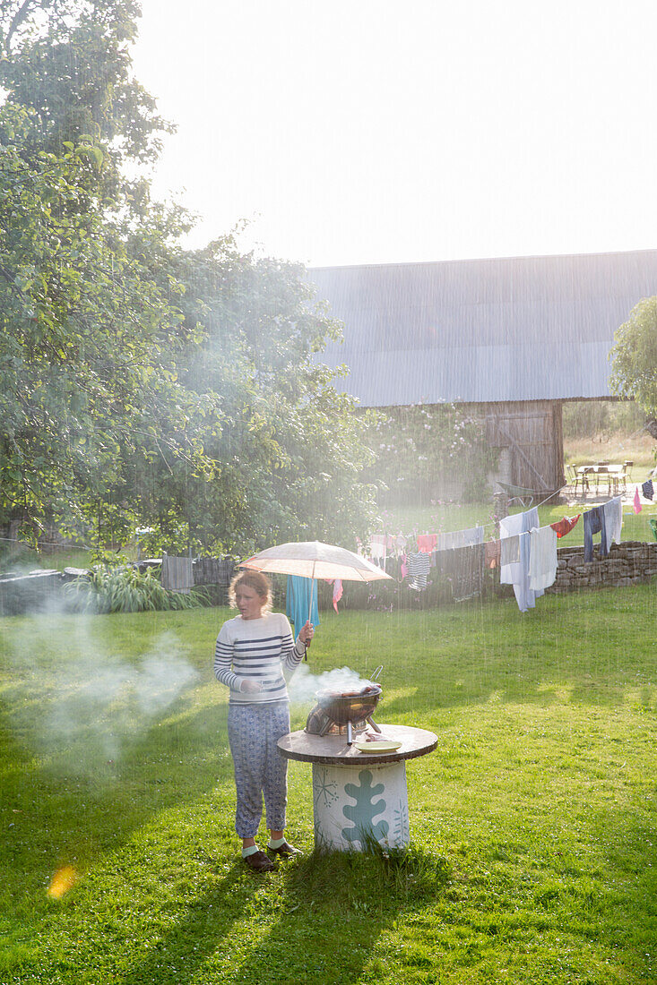 Girl with umbrella having barbecue in garden