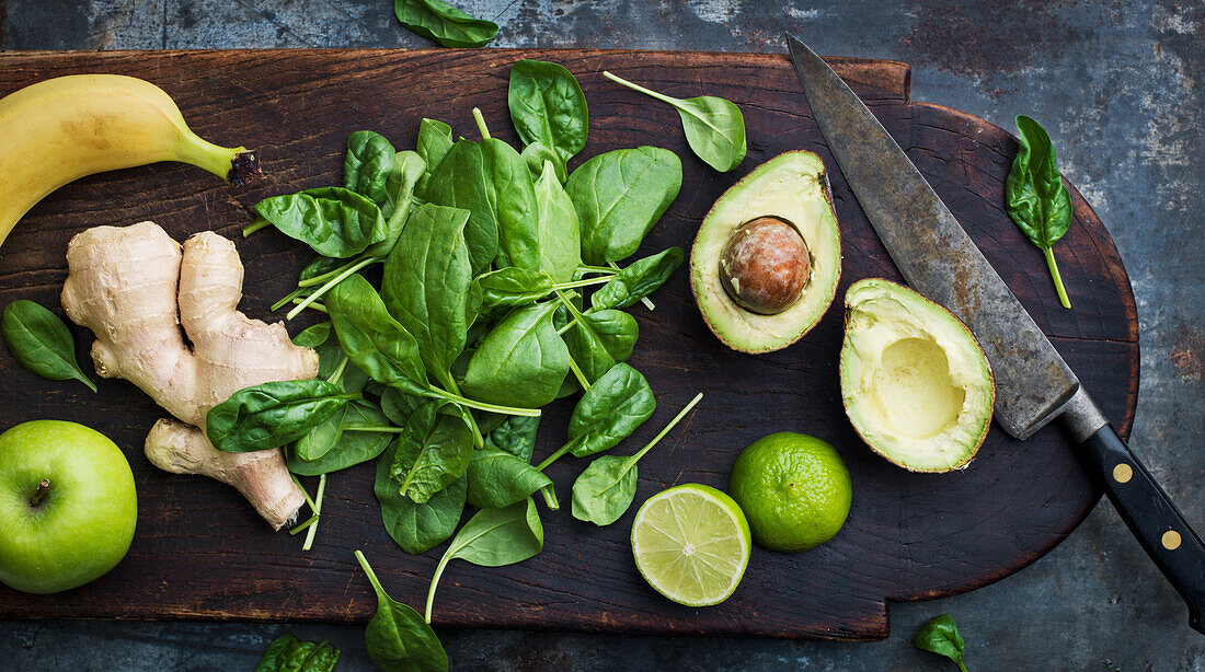 Avocado, Spinat, Ingwer, Apfel und Banane auf einem Schneidebrett