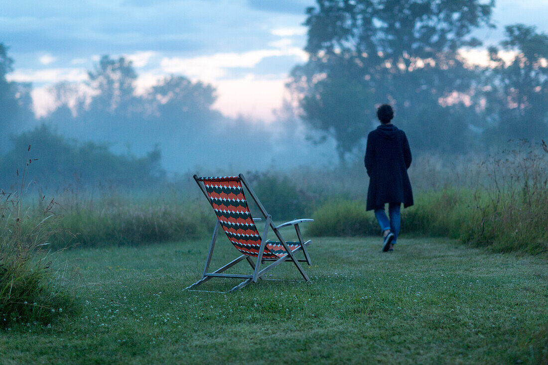 Empty sun chair at dusk, woman on background