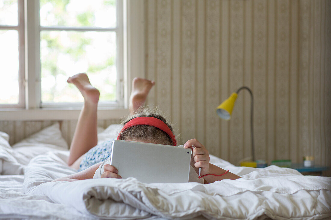 Mädchen liegt auf dem Bett und benutzt ein Tablet