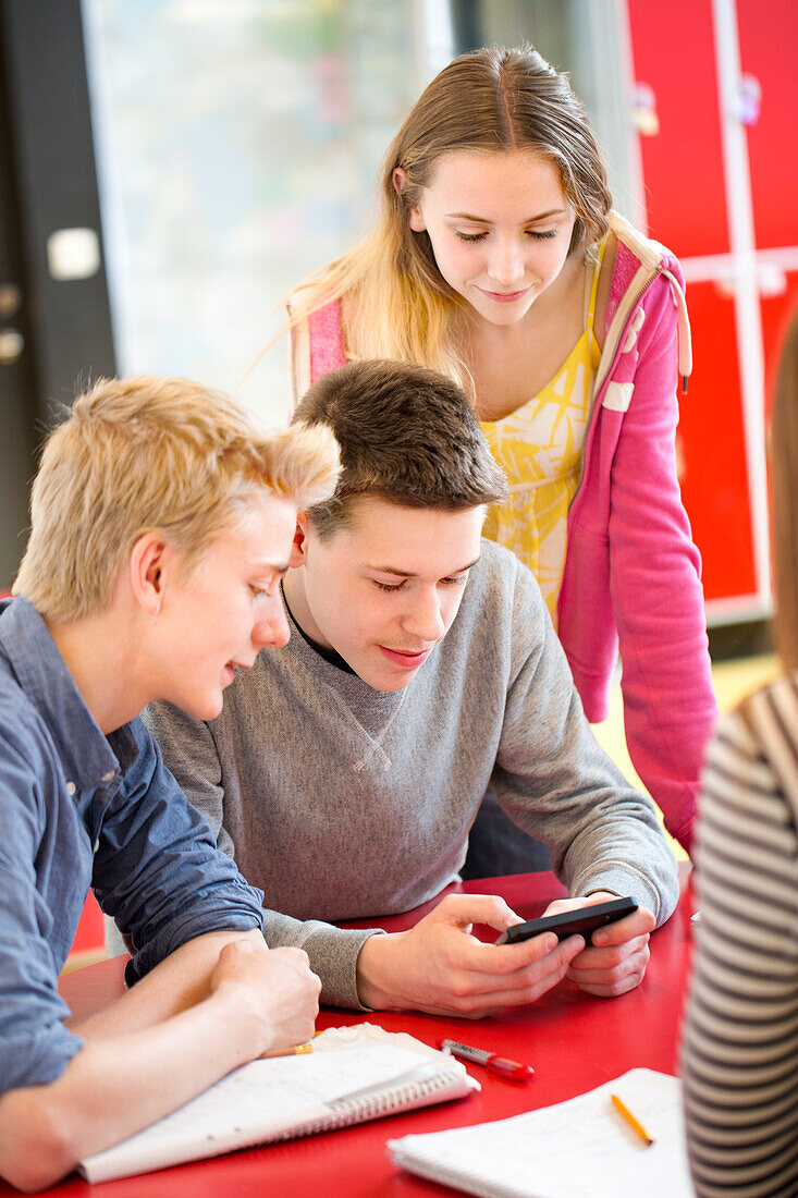 Teenager schauen auf ein Handy im Klassenzimmer