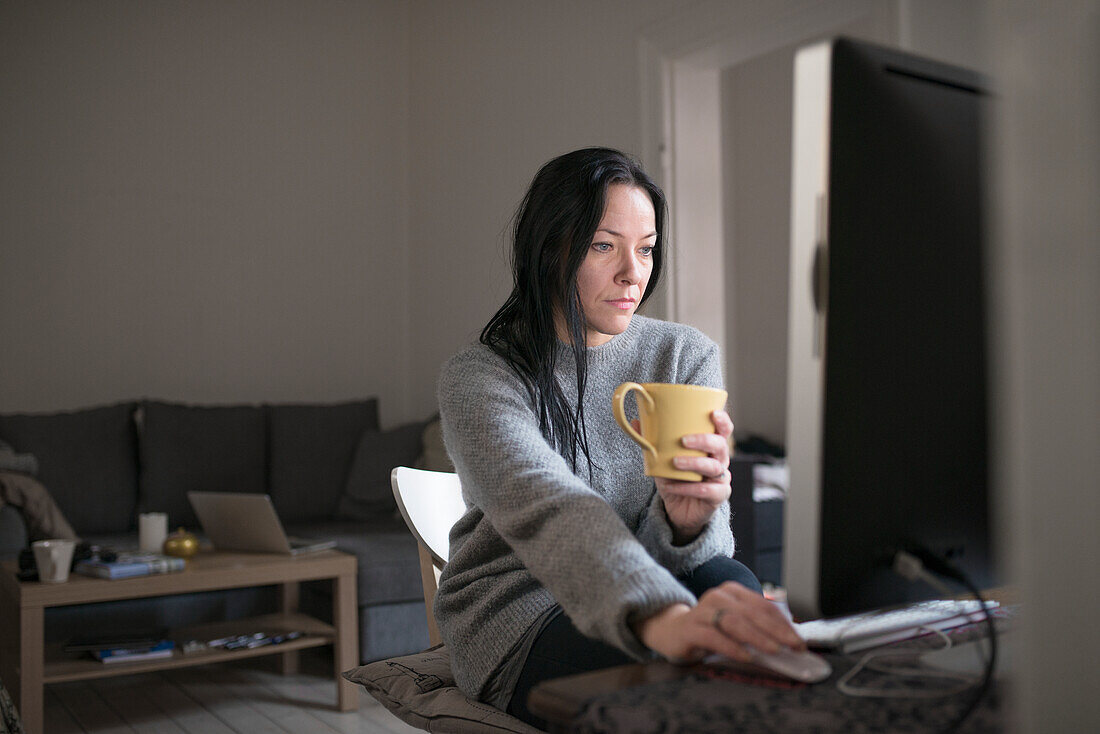 Frau mit Tasse, die einen Computer benutzt