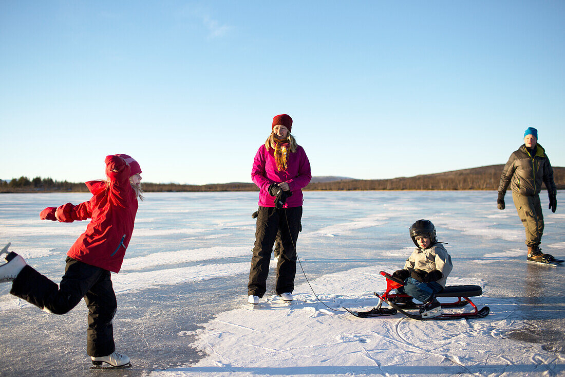 Mutter mit Kindern beim Schlittschuhlaufen am See