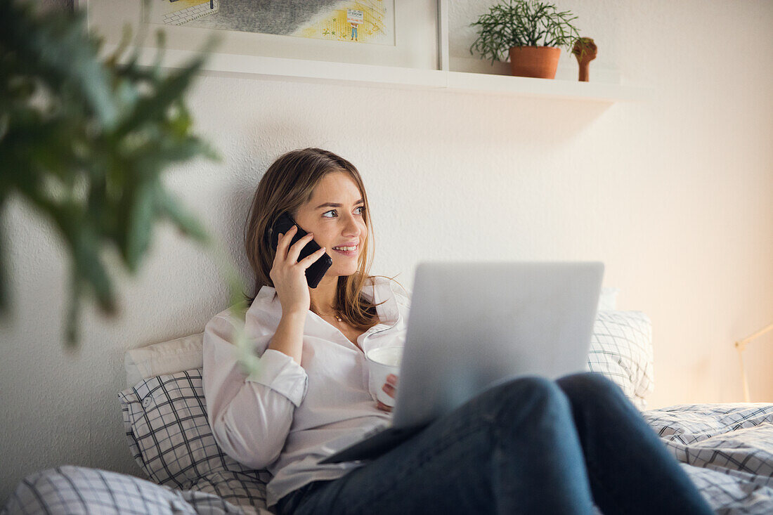 Young woman talking via phone in bed