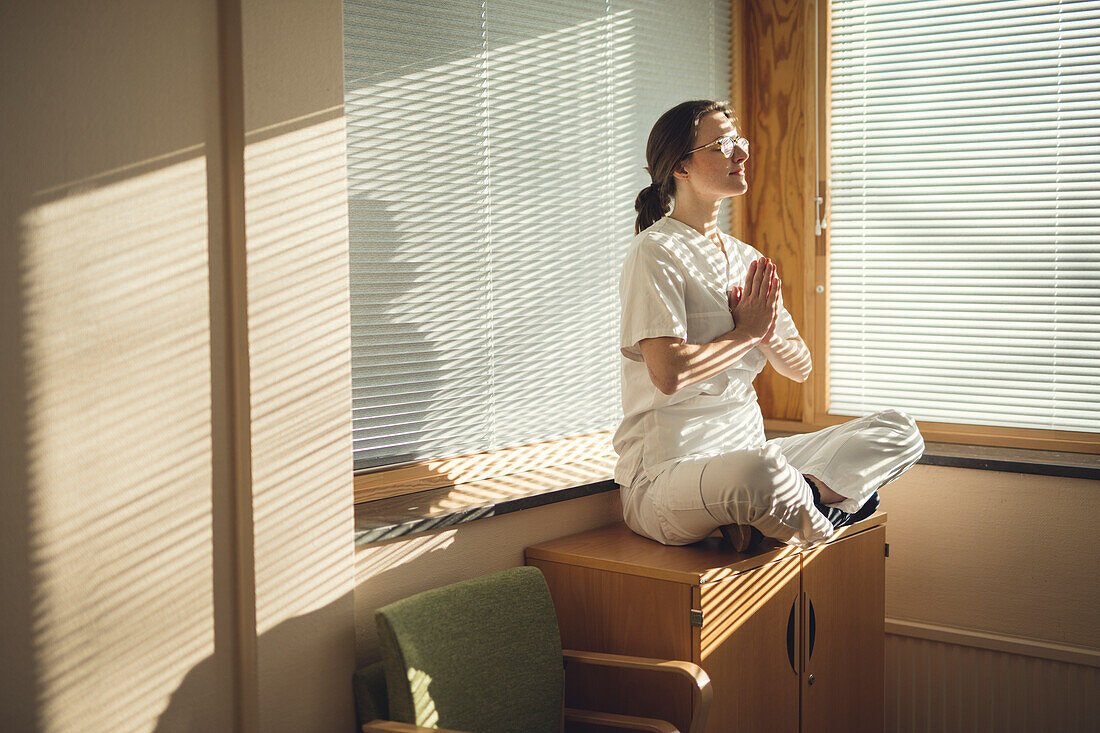 Ärztin meditiert am Fenster