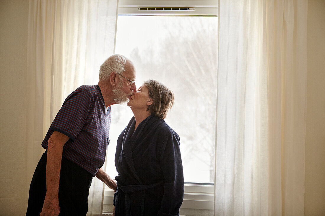 Senior couple kissing next to window