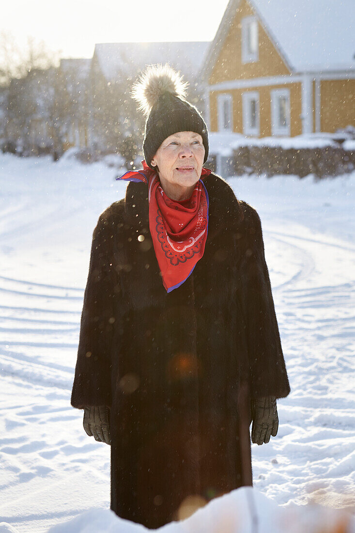 Ältere Frau steht im Winter vor dem Haus