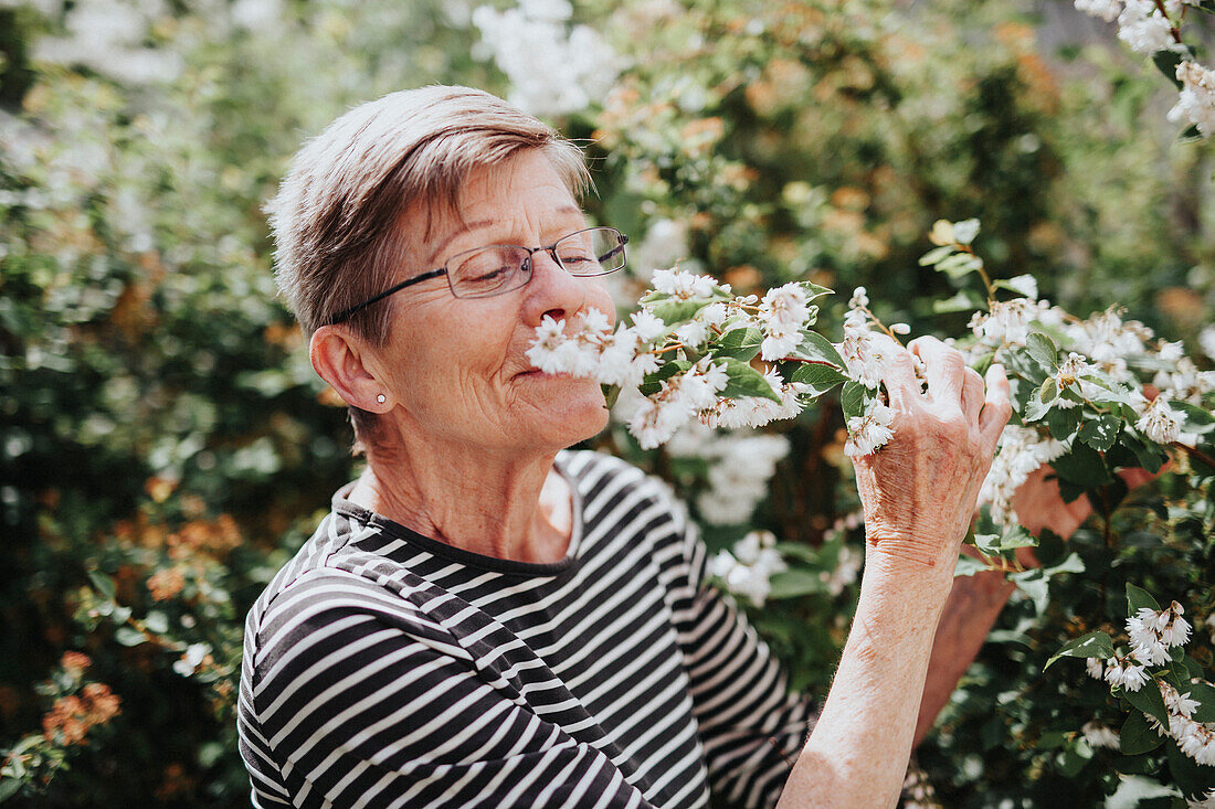 Ältere Frau riecht an Blumen im Garten