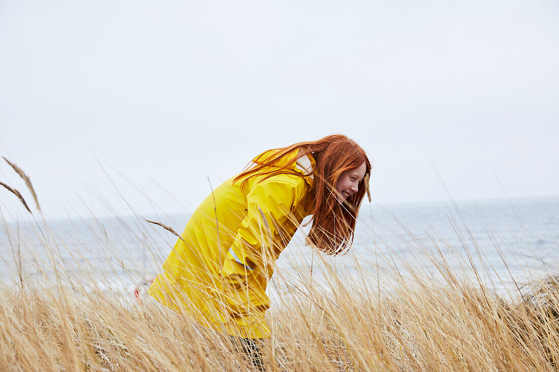 Fröhliches Mädchen in gelbem Regenmantel am Meer
