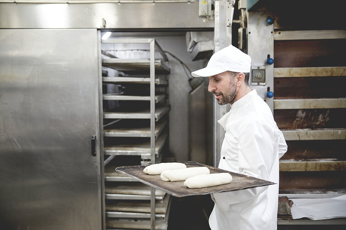 Baker holding dough on baking tray in kitchen