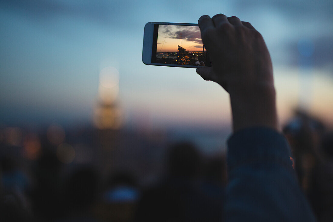 Person photographing skyscraper with smartphone at sunset