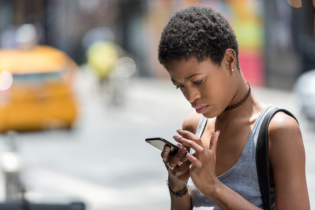 Porträt einer jungen Frau, die eine SMS auf einem Mobiltelefon schreibt