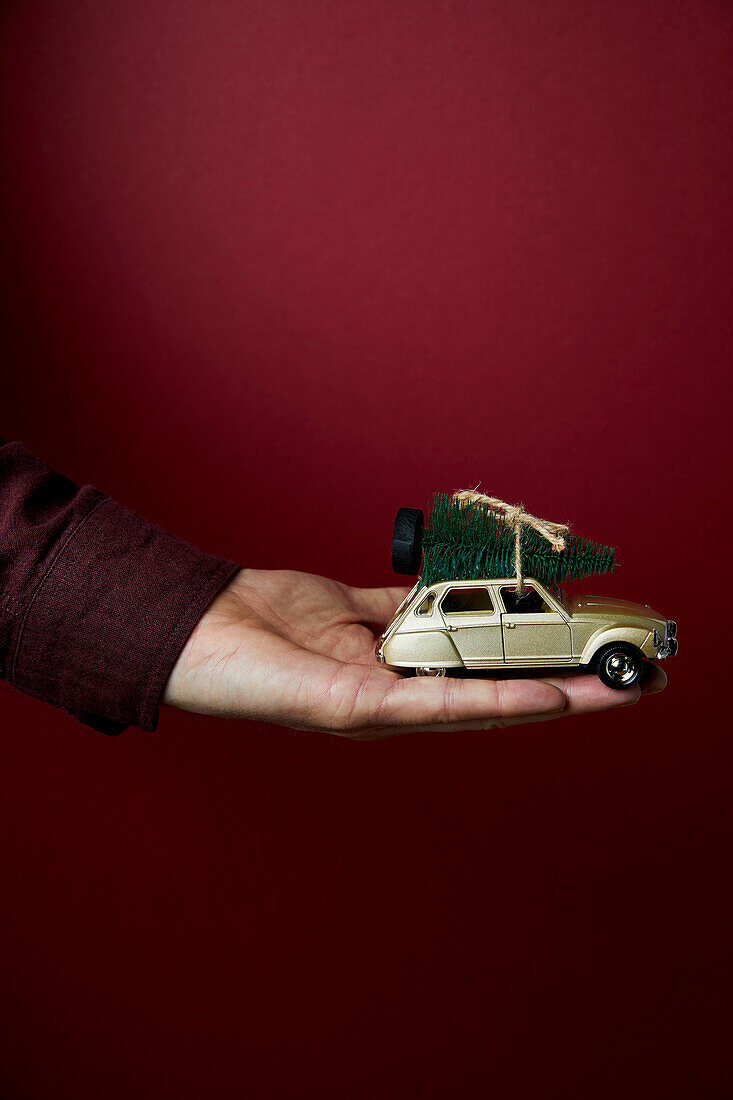 Hand hält Spielzeugauto mit Weihnachtsbaum in der Hand