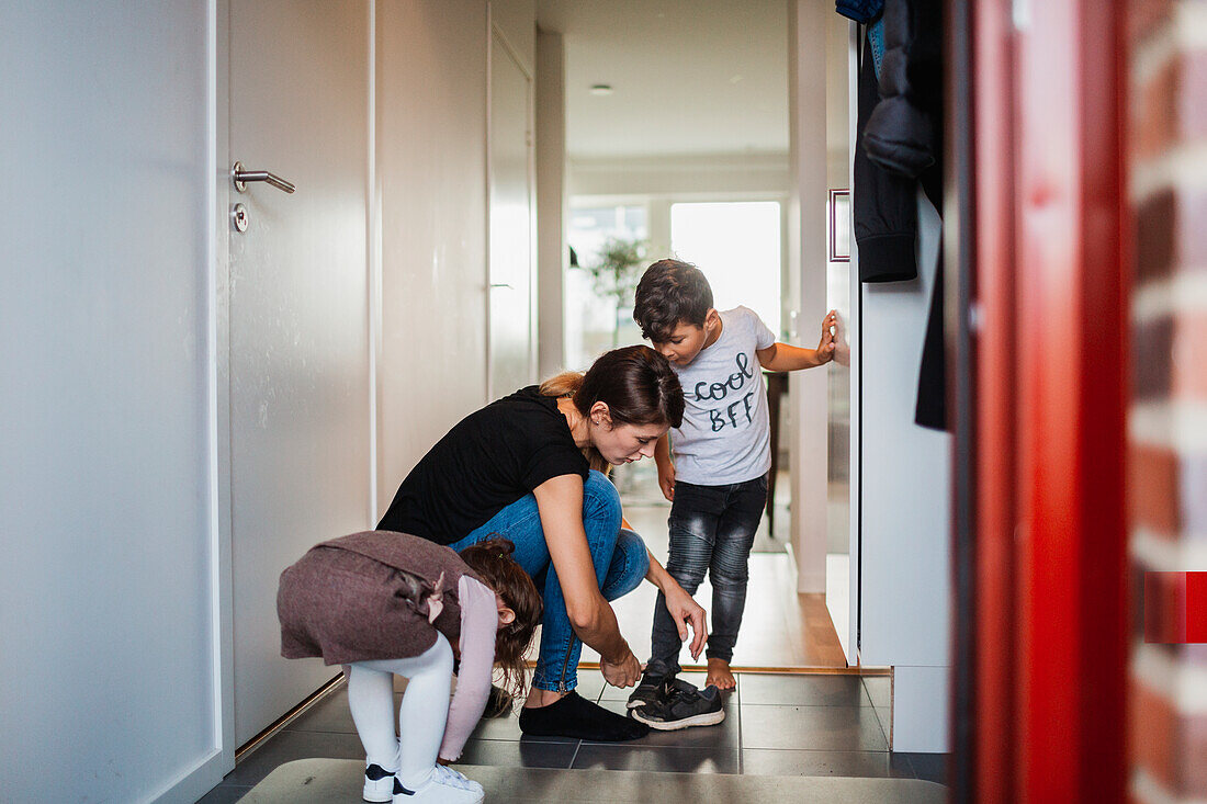 Mother and kids putting on shoes in entrance hall