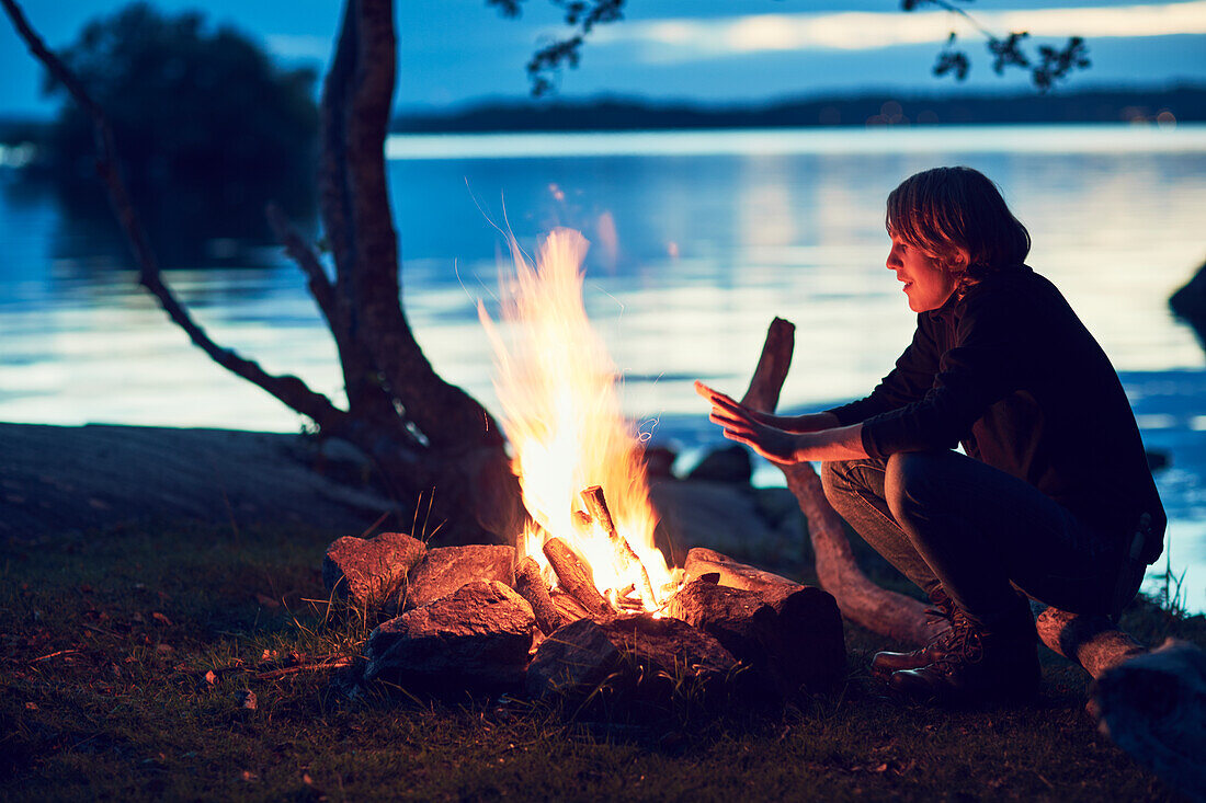 Young woman crouching next to campfire