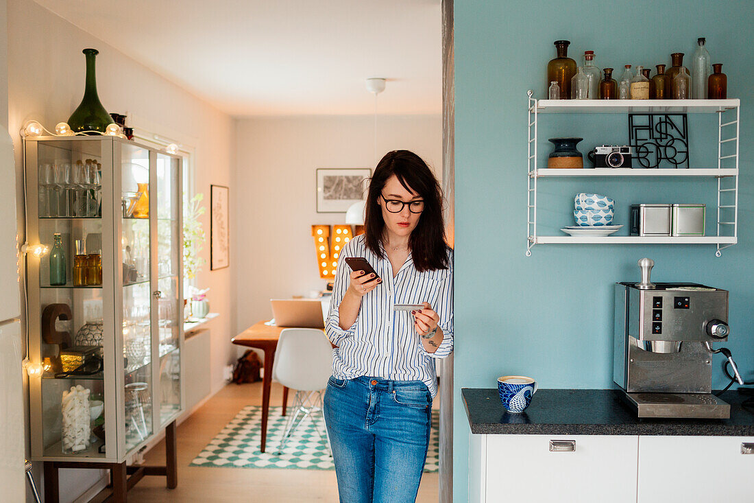 Young woman with smartphone and credit card in kitchen