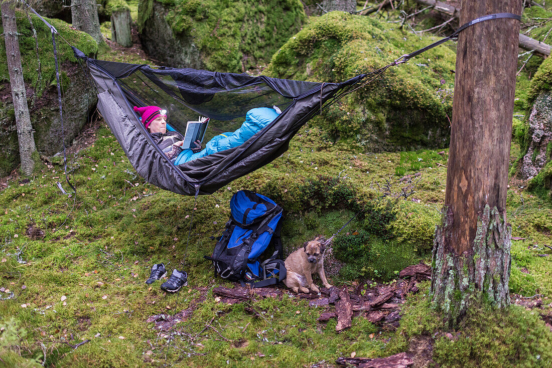 Frau liest Buch in Hängematte im Wald