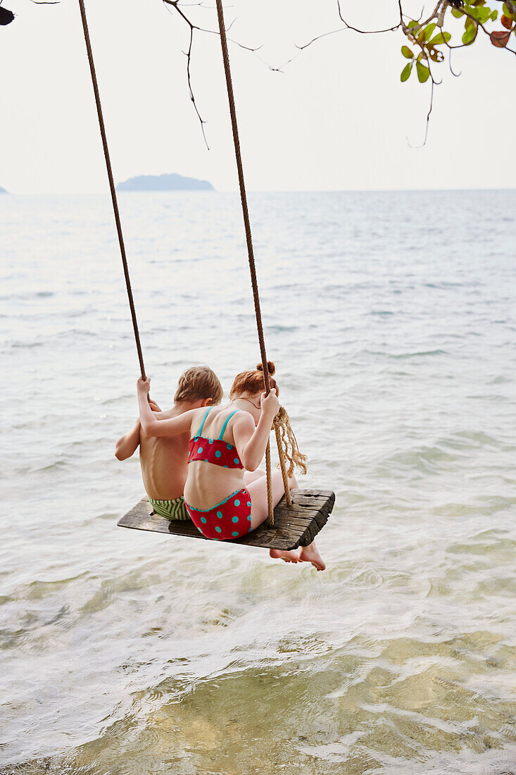 Boy and girl on swing at sea