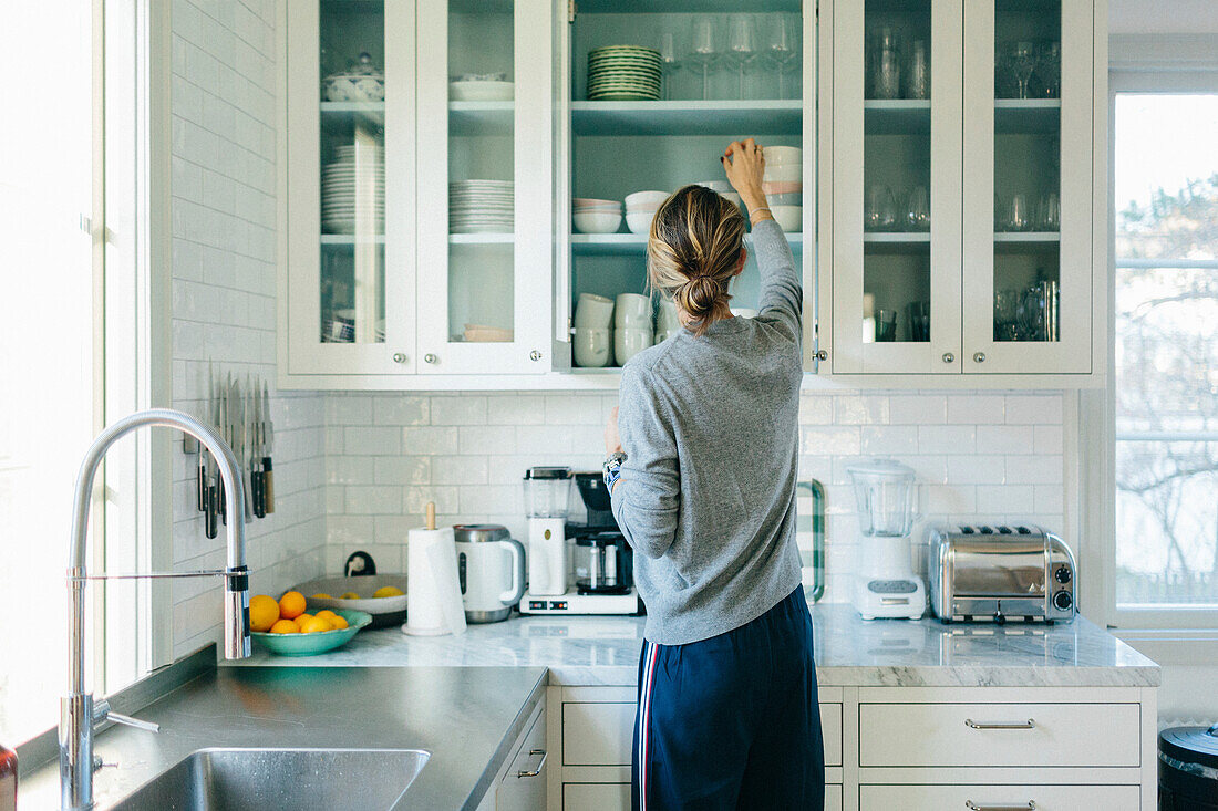 Woman reaching for bowl from kitchen cupboard