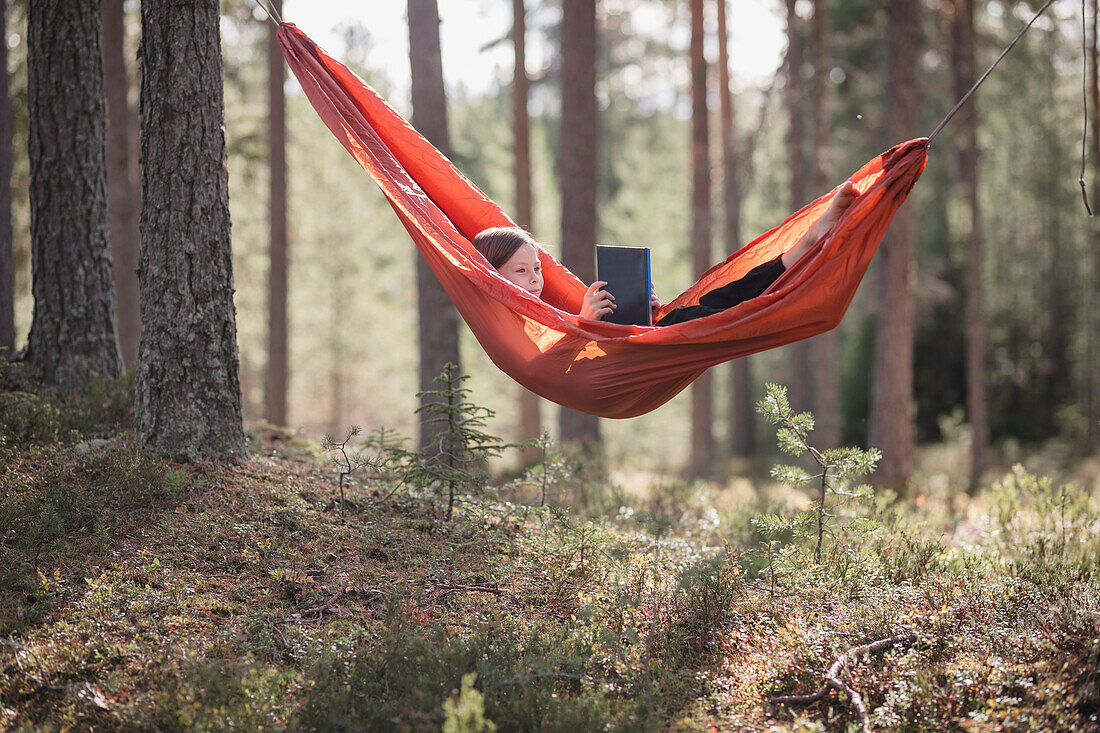 Teenager-Mädchen liest ein Buch in der Hängematte im Wald