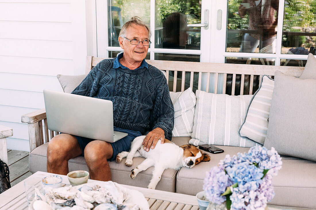 Man using laptop, sitting next to dog on sofa