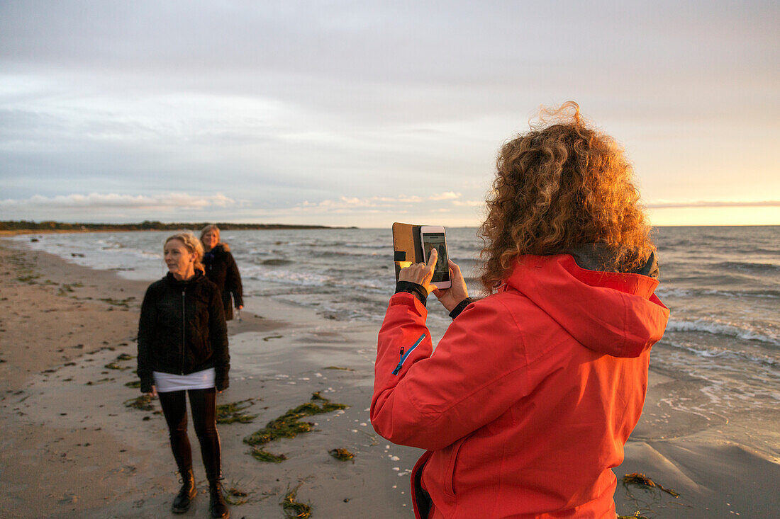 Frau fotografiert Freunde am Strand mit ihrem Smartphone