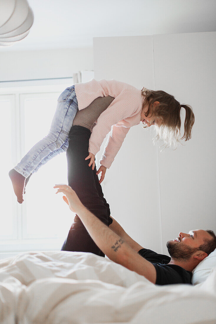 Father playing with daughter in bed