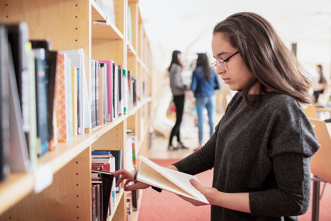 Teenager-Mädchen liest ein Buch in der Nähe eines Bücherregals