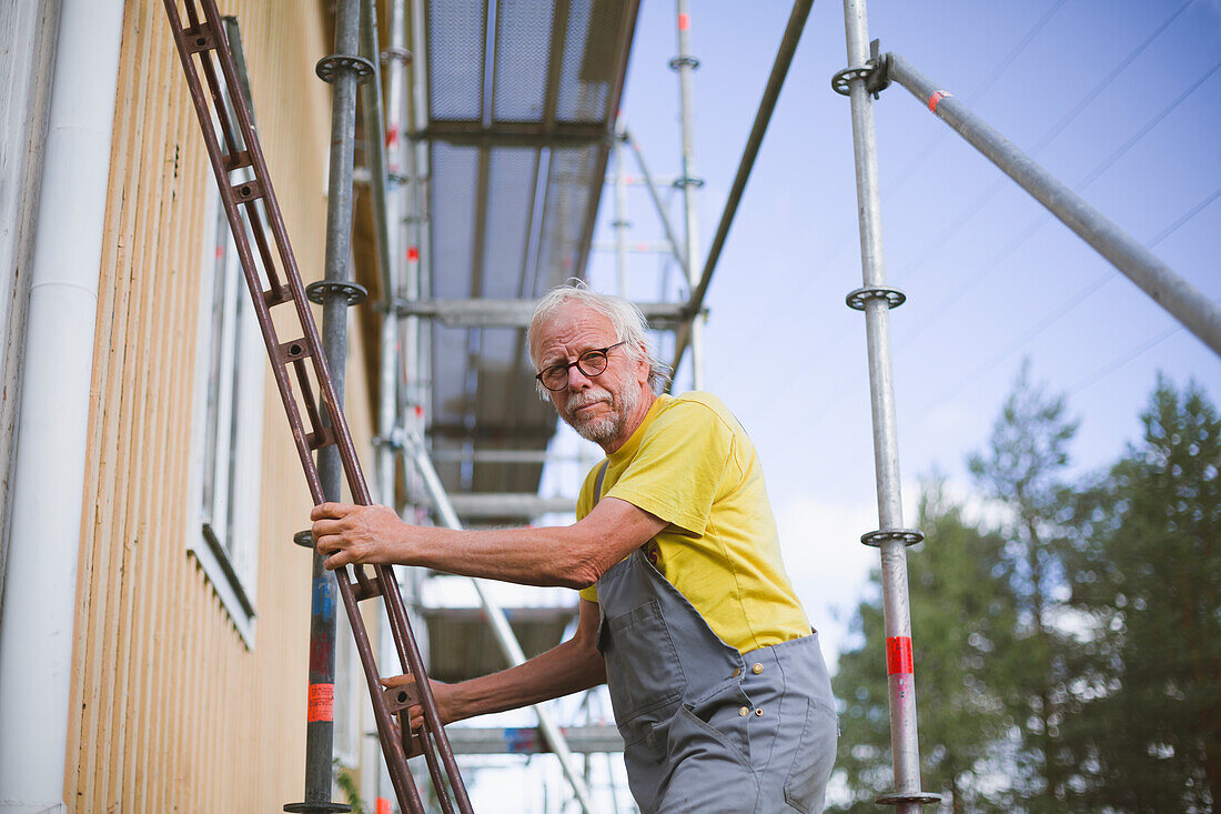 Älterer Mann steht auf einer Leiter