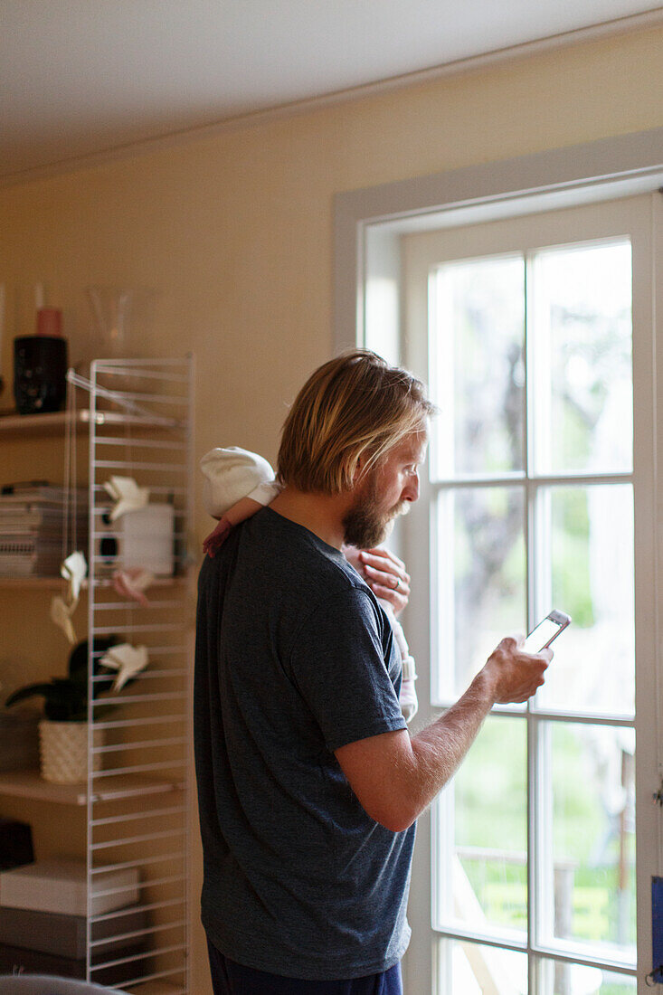 Father carrying baby and using phone