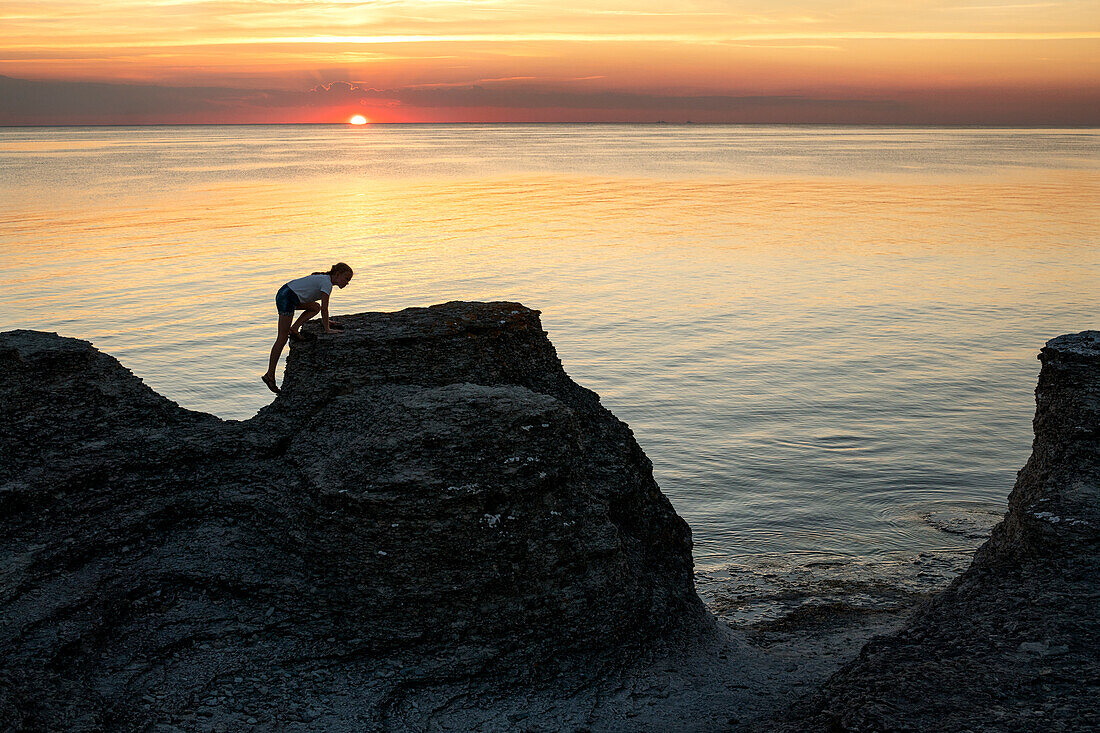 Mädchen klettert auf Felsen im Meer