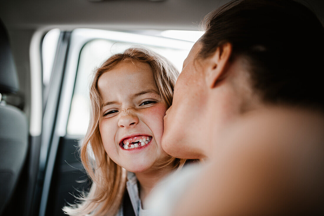 Happy daughter kissed by mother looking at camera