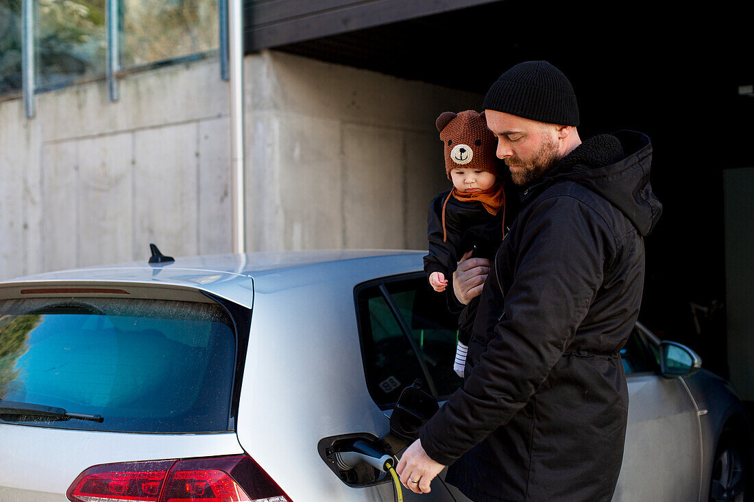 Man charging electric car while carrying baby